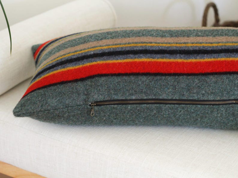 May include: A striped throw pillow with a zipper closure. The pillow is made of a soft, fuzzy fabric and has a green, red, yellow, and blue color scheme.