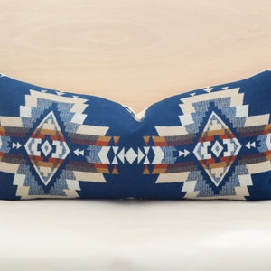May include: A blue and white patterned cushion with a geometric design. The cushion has a diamond shape in the centre with a red, orange, and brown border.