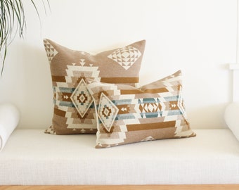 May include: Two decorative throw pillows with a geometric pattern in shades of brown, beige, and blue. The pillows are on a white linen couch.