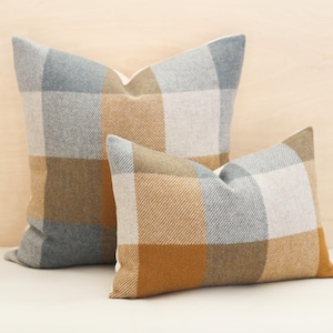 May include: Two plaid cushion covers, one larger than the other, with a brown, grey, and white plaid pattern. The cushions are made of a soft, textured fabric.