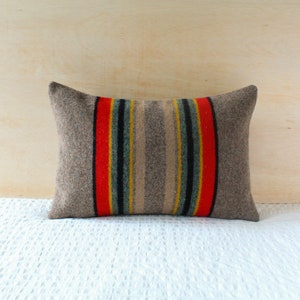 May include: A grey pillow with red, yellow and blue stripes. The pillow is made of a soft, woven fabric.