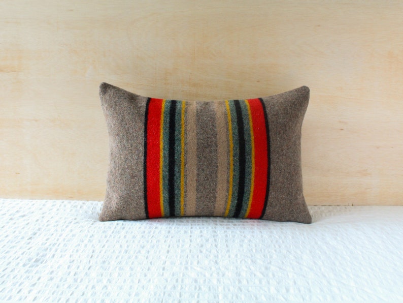 May include: A grey pillow with red, yellow and blue stripes. The pillow is made of a soft, woven fabric.