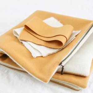 May include: A mustard yellow fabric pouch with a white zipper and a white lining. The pouch is folded in half and there are two pieces of white fabric inside.