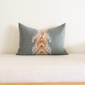May include: A rectangular decorative pillow with a gray background and a geometric design in shades of beige and orange. The pillow is resting on a white surface.