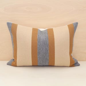 May include: A striped throw pillow with beige, brown, and grey stripes. The pillow is made of a soft, textured fabric.