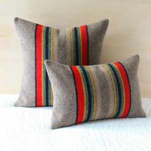 May include: Two decorative throw pillows with a striped pattern in shades of grey, red, yellow, and blue. The pillows are made of a soft, textured fabric.