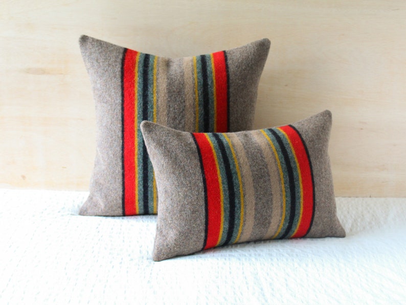 May include: Two decorative throw pillows with a striped pattern in shades of grey, red, yellow, and blue. The pillows are made of a soft, textured fabric.