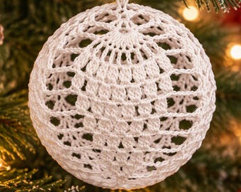 Op de afbeelding: Een bolvormig wit gehaakt ornament met een ingewikkeld opengewerkt patroon van onderling verbonden lussen en steken. De ronde, lichtgewicht decoratie hangt aan een dun bijpassend wit touwtje en toont een gedetailleerde handgemaakte textuur.