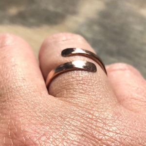 May include: A copper ring with a hammered finish, wrapped around a finger.