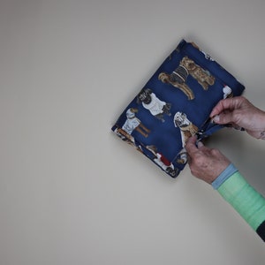 Può includere: Una pochette in tessuto blu con chiusura a zip. Il tessuto presenta un motivo di cani che indossano maglioni e cappelli.