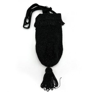 Può includere: Una borsa da sera nera a perline con un pon pon. La borsa è realizzata con piccole perline nere e ha una lunga tracolla a perline.