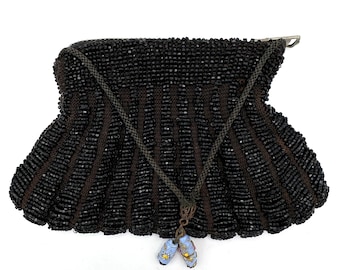 May include: A black beaded purse with a drawstring closure and a tassel. The purse is made of small, black beads and has a scalloped edge.