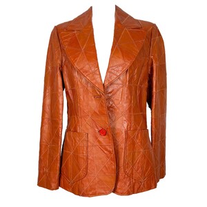 May include: A vintage brown leather blazer with a geometric pattern. The blazer has a notched collar, two front pockets, and a single red button closure. The jacket is a medium size.