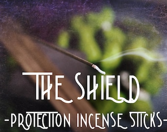 May include: White incense sticks with the text "THE SHIELD - PROTECTION INCENSE STICKS -" on a blurred background of green and purple.