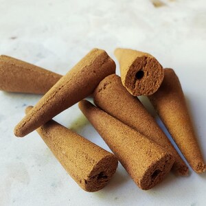 May include: A group of six brown incense cones, each with a small hole in the center. The cones are arranged in a pile on a white surface.