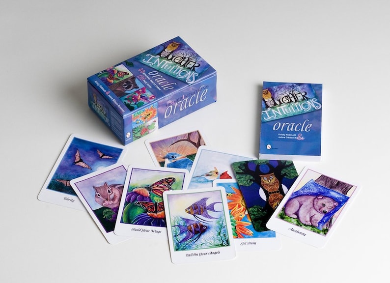 An oracle deck box, book, and sampling of included cards. The box is mostly blue-violet with Higher Intuitions Oracle on the front. Cards include images of bear, owls, angelfish, butterflies, chipmunk, bats, cardinals, bluebird, and bats.