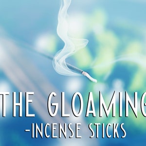 Pode incluir: Um pau de incenso branco com fuma&ccedil;a subindo sobre um fundo azul e verde desfocado. O texto "THE GLOAMING - INCENSE STICKS" est&aacute; abaixo do pau.