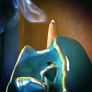 A close-up view of a blue ceramic object with a white tip, emitting smoke, against a blurred background.