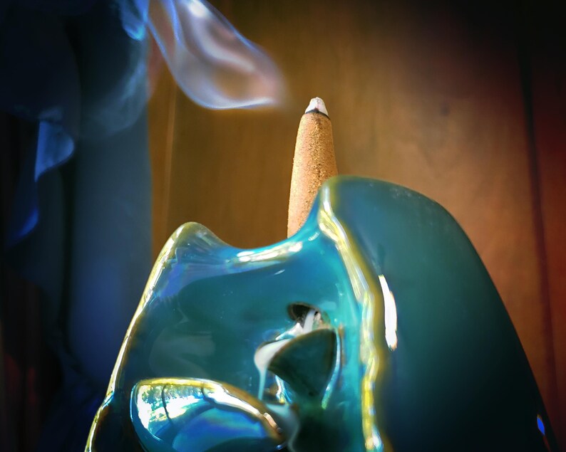 A close-up view of a blue ceramic object with a white tip, emitting smoke, against a blurred background.