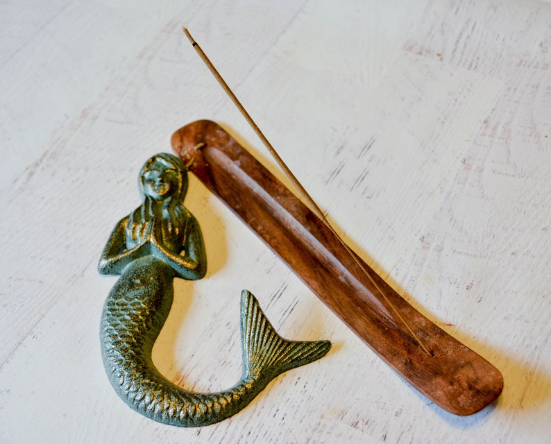 May include: A green mermaid figurine with a wooden incense holder and a stick of incense. The incense holder is brown and has a groove for the incense to sit in.