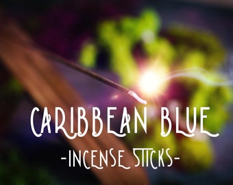 May include: A close-up of a smoldering incense stick with smoke rising from the end. The text "CARIBBEAN BLUE - INCENSE STICKS -" is visible in the foreground.