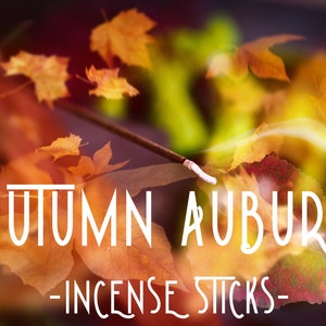 May include: An image featuring the text "AUTUMN AUBURN - INCENSE STICKS" in white, stylized font. The background is a blur of autumn leaves in shades of orange and yellow, with a lit incense stick emitting smoke.