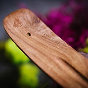 May include: A wooden incense burner with a small hole in the center. The burner is made of a light brown wood with a smooth finish.