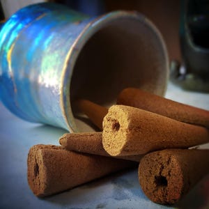 Pode incluir: Um close-up de um monte de cones de incenso marrons. Os cones est&atilde;o dispostos em uma pilha, com as pontas dos cones apontando para cima. Os cones s&atilde;o feitos de um material marrom escuro e t&ecirc;m uma textura ligeiramente &aacute;spera.