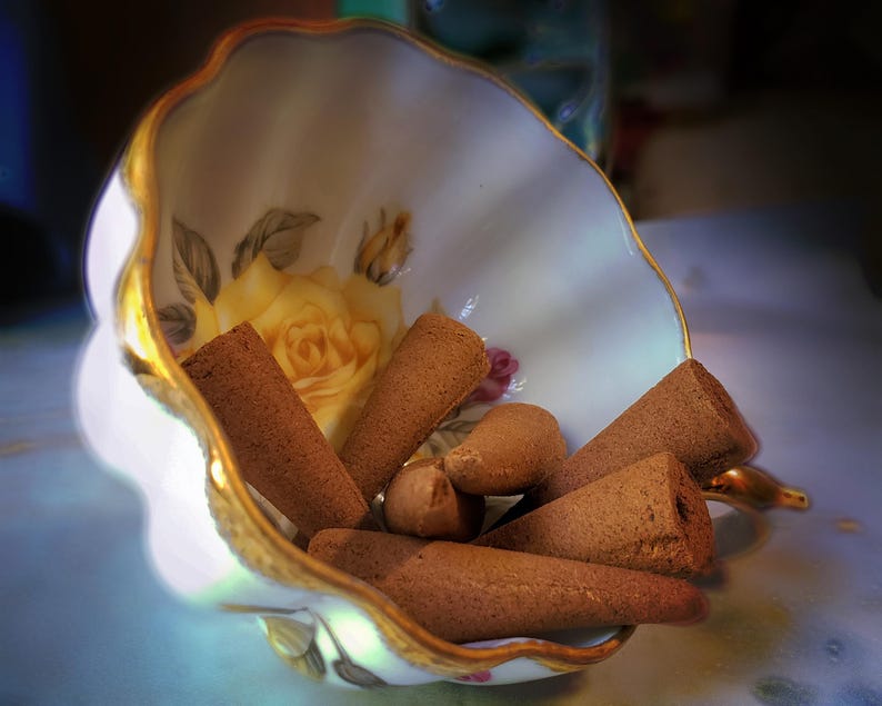 Puede incluir: Una taza de t&eacute; vintage llena de conos de incienso marrones. La taza es blanca con un borde dorado y un dise&ntilde;o de rosa amarilla. Los conos de incienso son de varios tama&ntilde;os y formas.