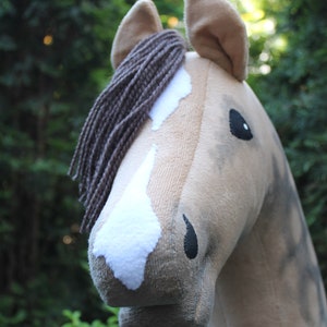 May include: A plush horse head with a brown mane, white markings, and black eyes. The horse is a light brown color and has a soft, fuzzy texture.