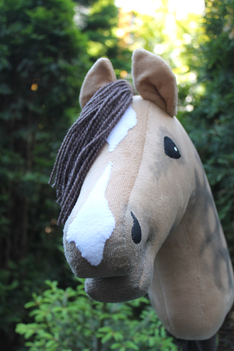 May include: A plush horse head with a brown mane, white markings, and black eyes. The horse is a light brown color and has a soft, fuzzy texture.