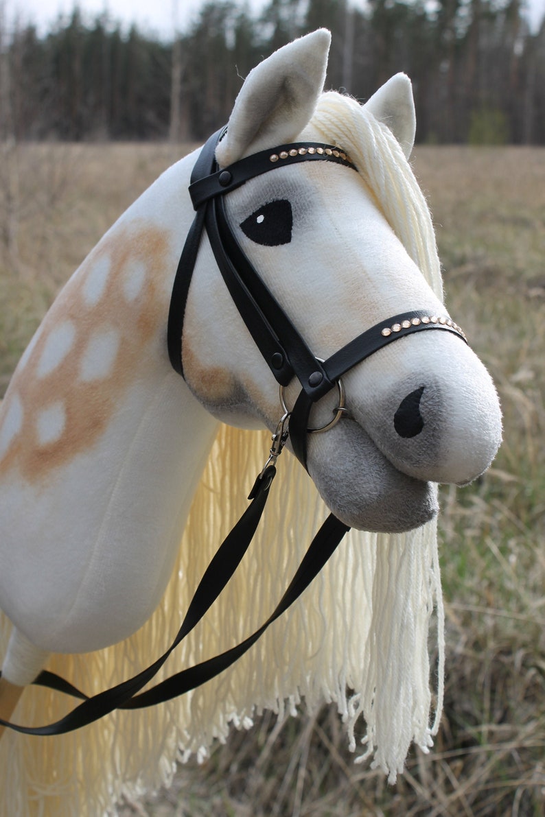 May include: A white and brown rocking horse with a black bridle and reins. The horse has a long white mane and tail.