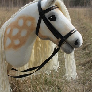 May include: A white and brown rocking horse with a black leather bridle and a white mane and tail. The horse has a black leather strap attached to the bridle.