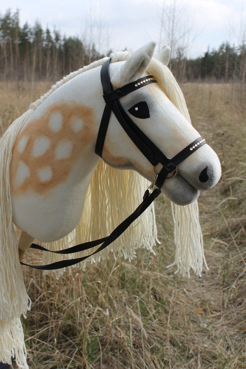 May include: A white and brown rocking horse with a black leather bridle and a white mane and tail. The horse has a black leather strap attached to the bridle.