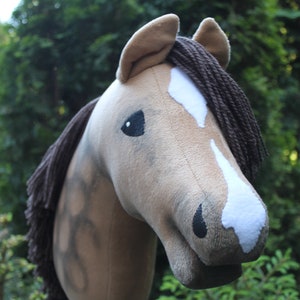 May include: A brown and white plush horse head with a brown mane. The horse has a black nose and eyes.