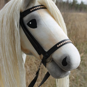 May include: A white stuffed horse head with a black leather bridle and a row of gold rhinestones. The horse has a white mane and tail.
