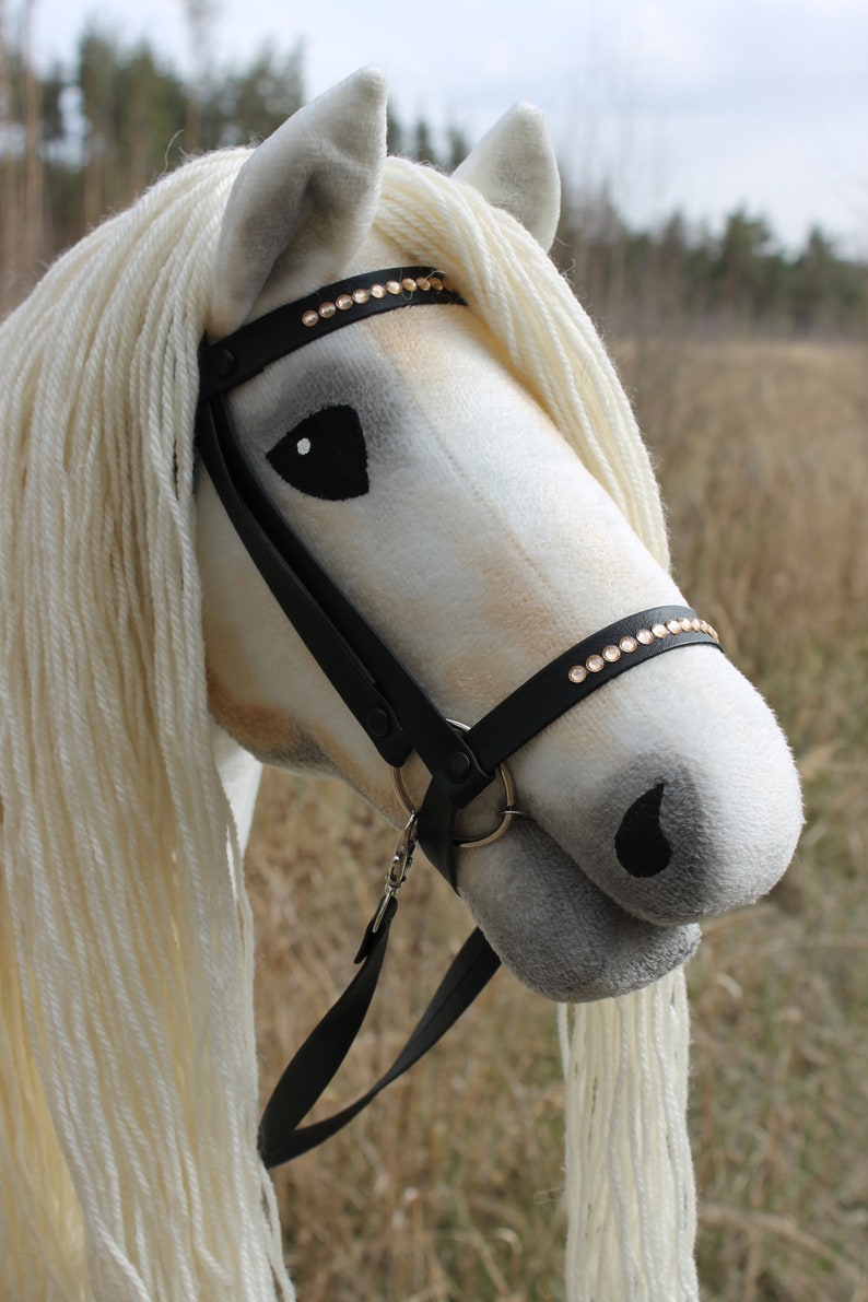 May include: A white stuffed horse head with a black leather bridle and a row of gold rhinestones. The horse has a white mane and tail.