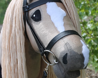 May include: A plush horse head with a black leather bridle and a white star on its forehead. The horse has a long, cream-colored mane and tail.