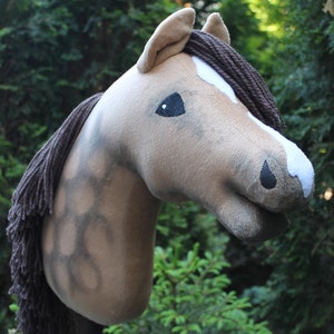 May include: A brown and white horse head with a brown mane, used as a hobby horse. The horse head is made of plush fabric and has a stitched-on black eye.