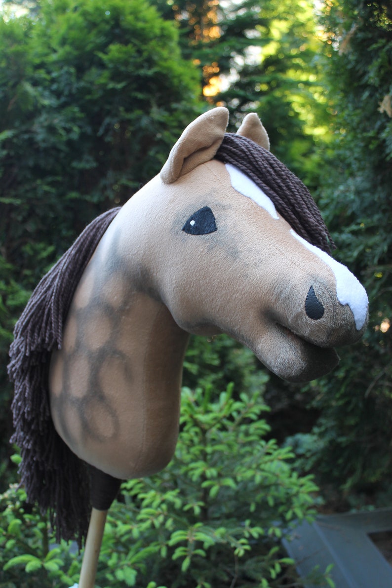 May include: A brown and white horse head with a brown mane, used as a hobby horse. The horse head is made of plush fabric and has a stitched-on black eye.