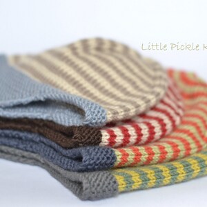 May include: A stack of five knitted hats in various colors and patterns, including blue, brown, red, orange, and yellow. The hats are striped and have a textured knit. The text "Little Pickle Knits" is visible in the top right corner of the image.