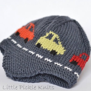 Könnte beinhalten: Eine graue Strickmütze mit einem weißen Zickzack-Saum und bunten Automotiven. Die Autos sind rot, gelb und orange.