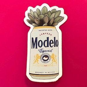May include: A sticker featuring a Modelo beer can with a succulent plant growing out of the top. The can is white with blue and gold accents, and the words "Modelo Especial" are prominently displayed. The background is a solid magenta color.