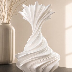 May include: A white, abstract decorative vase with a swirling, textured design. The vase has a flared base and a starburst-like top. A second, off-white vase and branches are in the background.