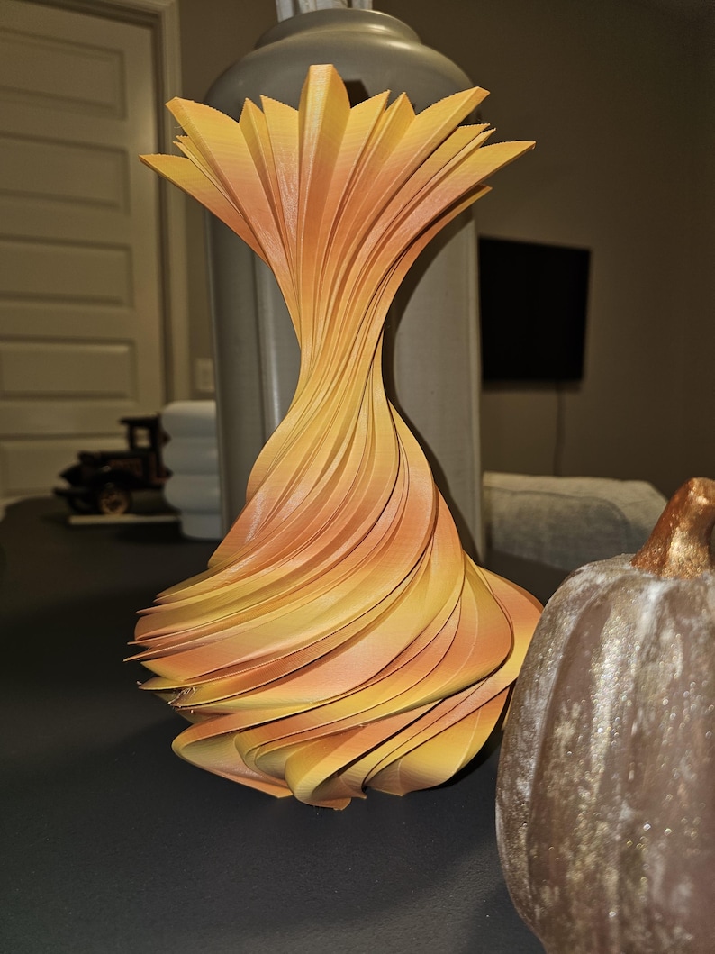 May include: A decorative, abstract vase with a unique, layered design. The vase features a spiral shape with alternating layers of yellow and orange hues. The vase is a modern home decor item.