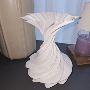 May include: A white, decorative vase with a unique, swirling design. The vase has a wide, flared top and a textured, layered base. The design is reminiscent of a flower. The vase is made of a solid, opaque material.