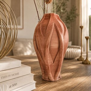 May include: A terracotta-colored vase with a textured, ribbed surface and a vertical, pleated design. The vase has a narrow neck and a wider, bulbous body, featuring a matte finish with visible horizontal lines throughout the structure.