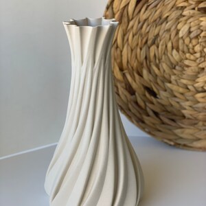 May include: A cream-colored vase with a unique, swirling design. The vase has a wide base that tapers to a narrow neck, with a ruffled top. The textured surface creates a dynamic visual effect. The vase is a decorative item.
