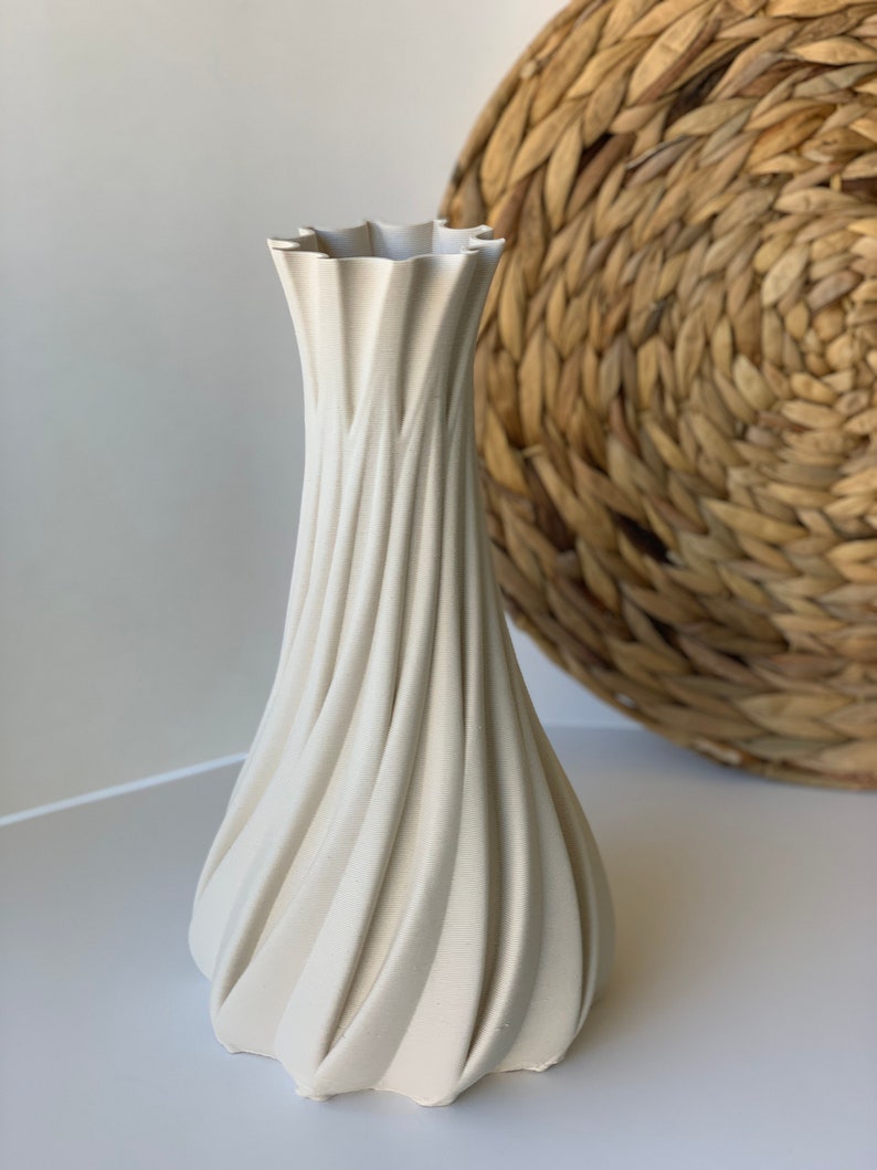 May include: A cream-colored vase with a unique, swirling design. The vase has a wide base that tapers to a narrow neck, with a ruffled top. The textured surface creates a dynamic visual effect. The vase is a decorative item.