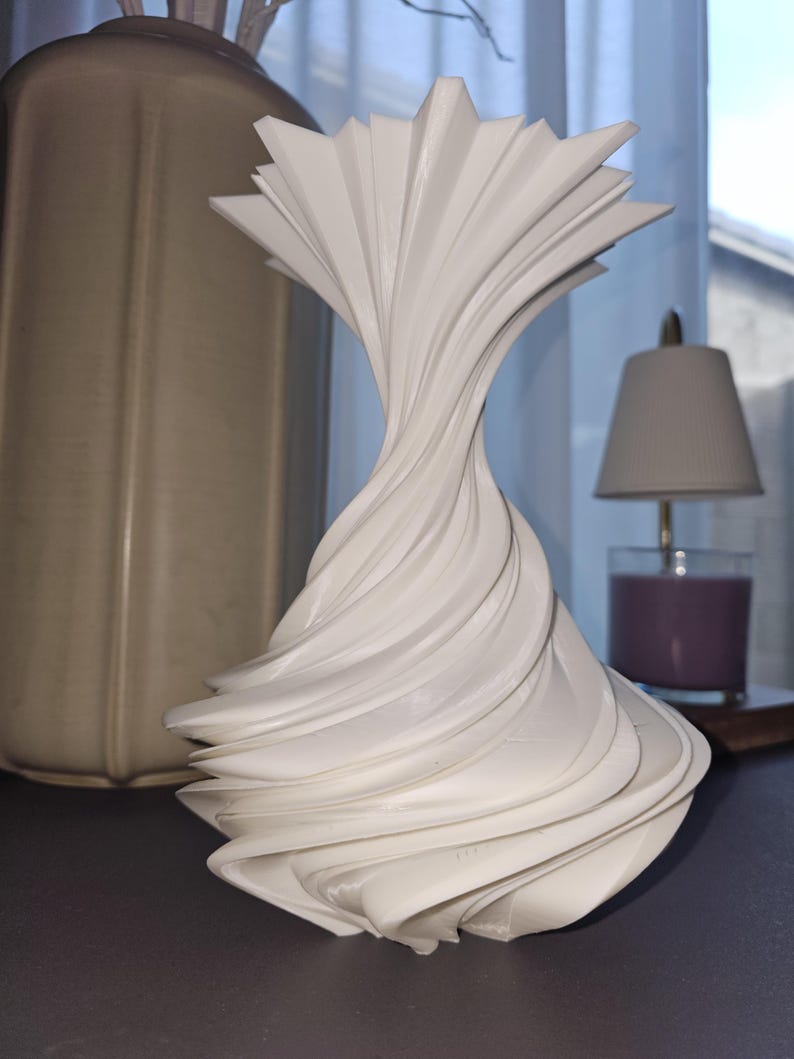 Cascade Elegance Vase by RemJDesign featuring a fluid, wave-like 3D printed design inspired by natural water movement. Crafted in premium PLA with a smooth matte finish, this modern sculptural vase showcases soft organic curves and minimalist form. Ideal for neutral or contemporary interiors, it serves as a decorative art piece or functional vase for dried or fresh flowers. Original modern home décor by RemJDesign.